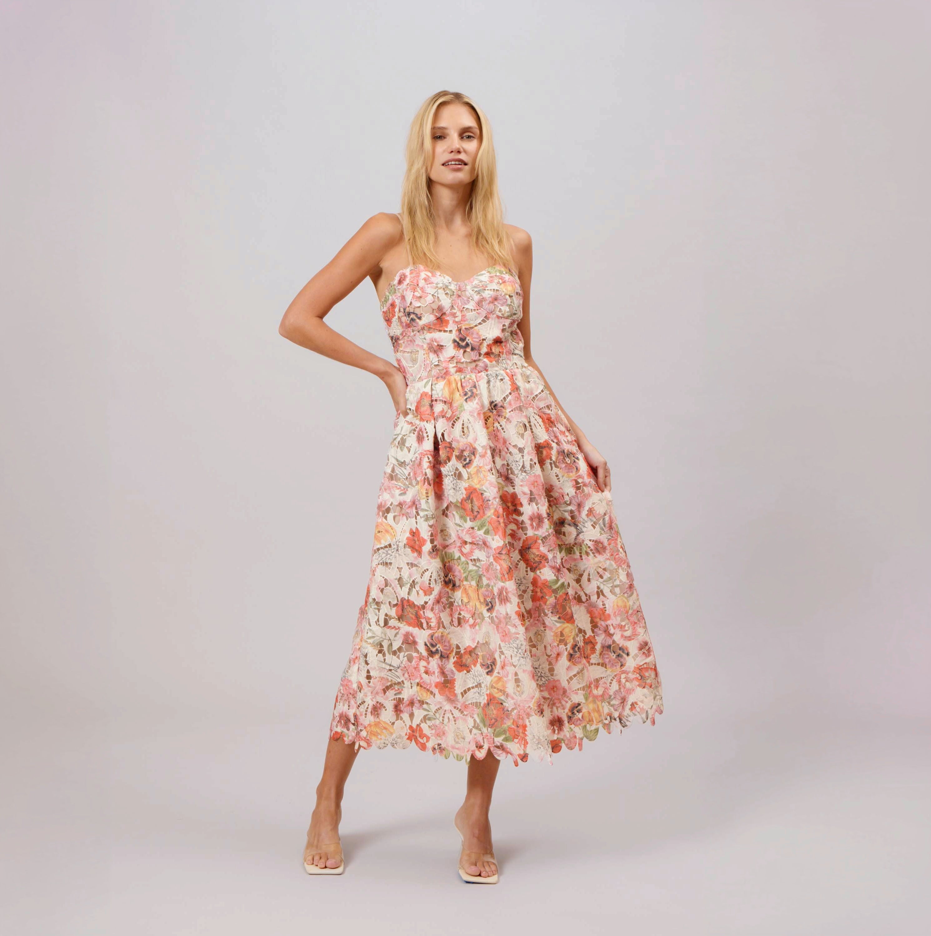 Woman wearing a strapless floral lace midi dress with a fitted bodice and flared skirt, styled with neutral heels, perfect for an elegant summer or spring event.
