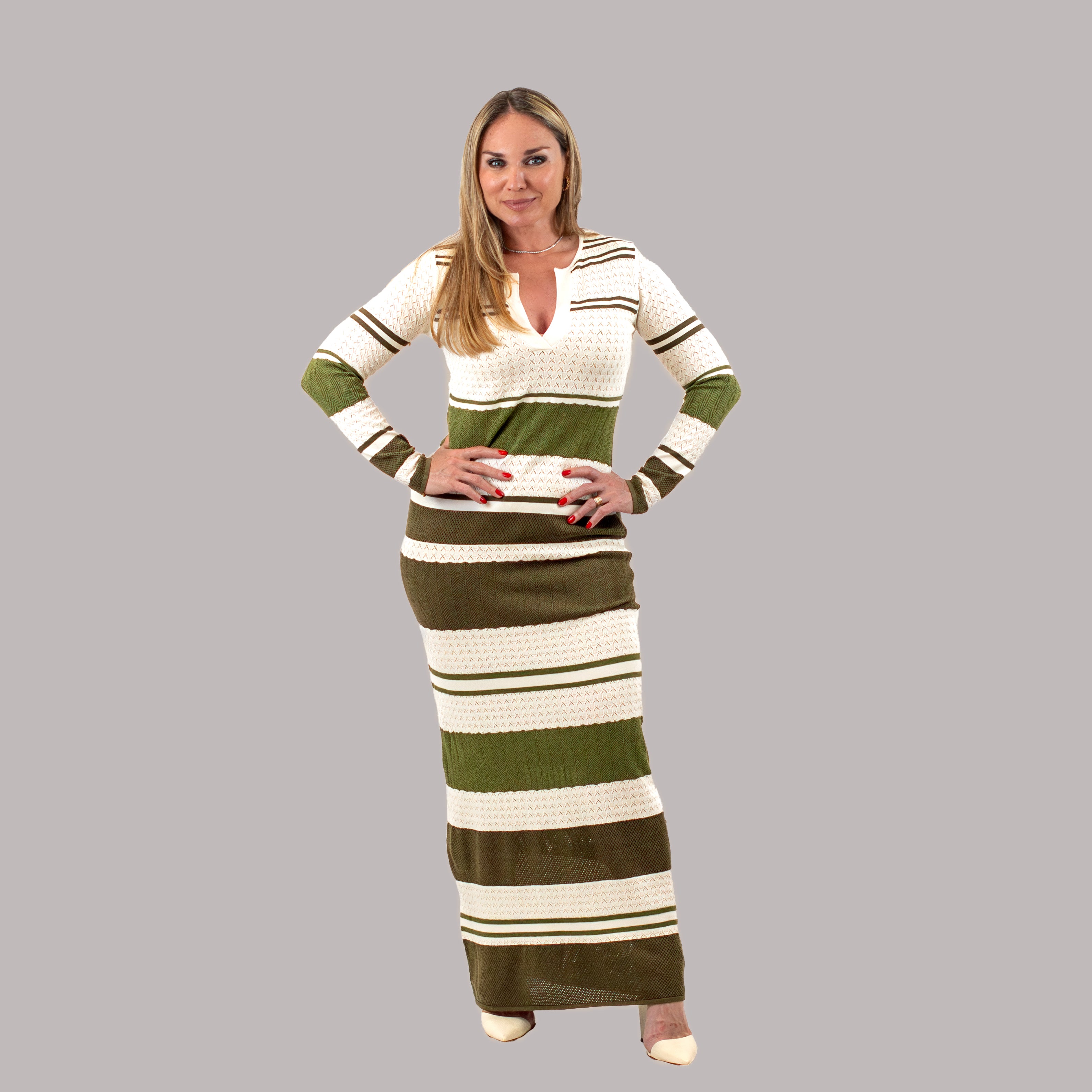 Full-length view of a woman in an olive green and cream striped knit maxi dress featuring a V-neckline and long sleeves, paired with beige heels.