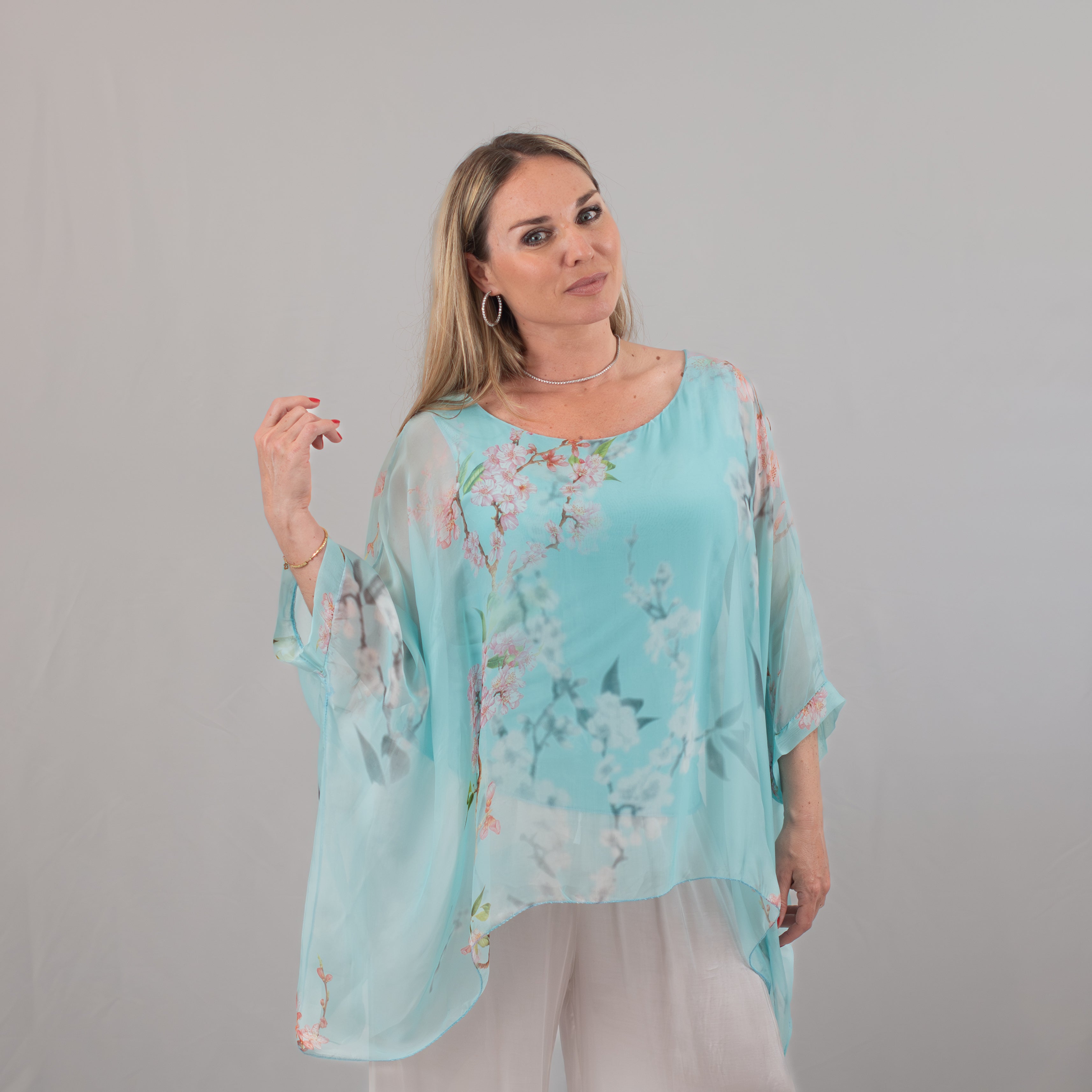 Woman in a light blue floral-print tunic with billowy sleeves, styled with white pants, showcasing the airy and elegant fit of the garment.