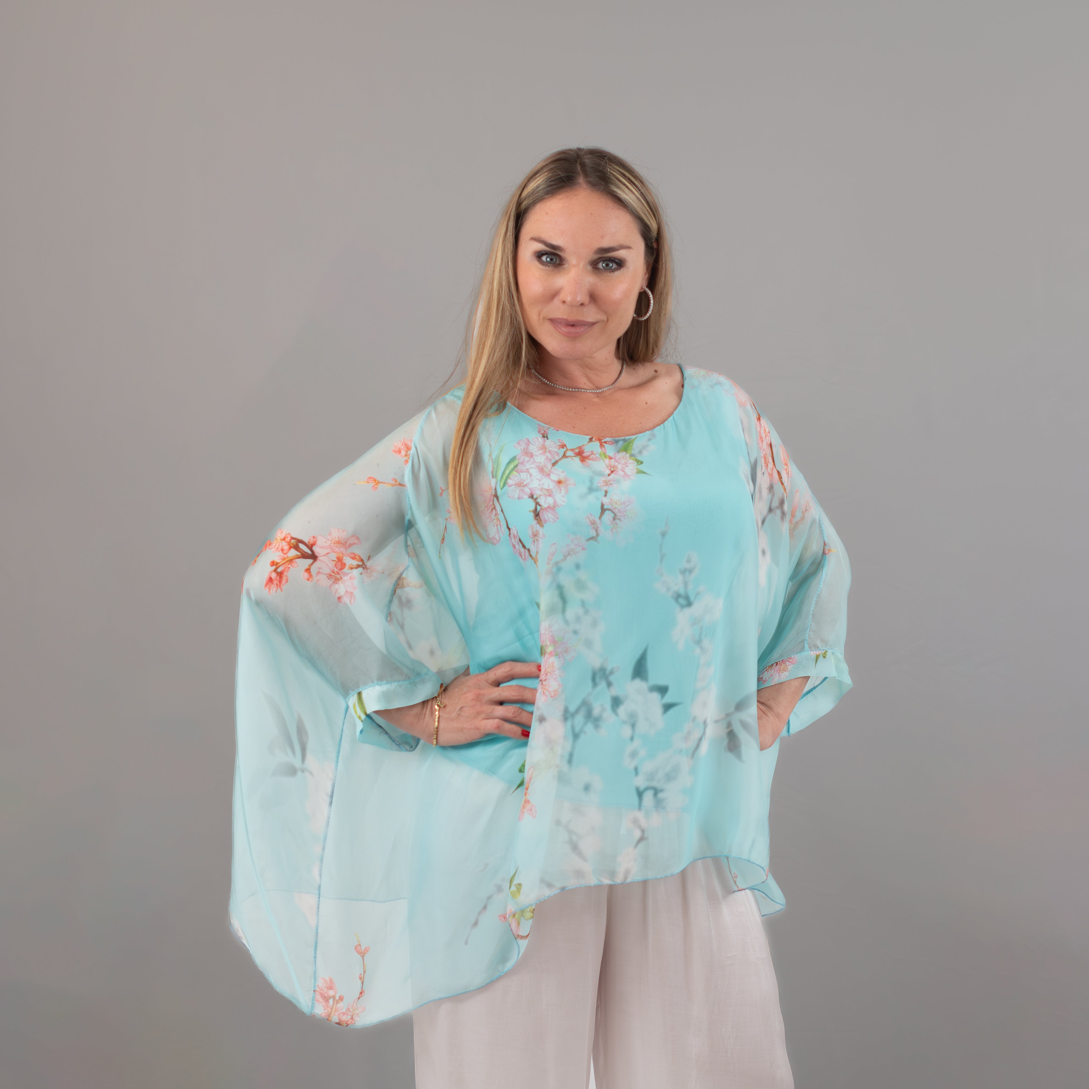 Woman wearing a flowy light blue tunic with a floral print design, paired with white pants, perfect for casual and elegant summer looks.