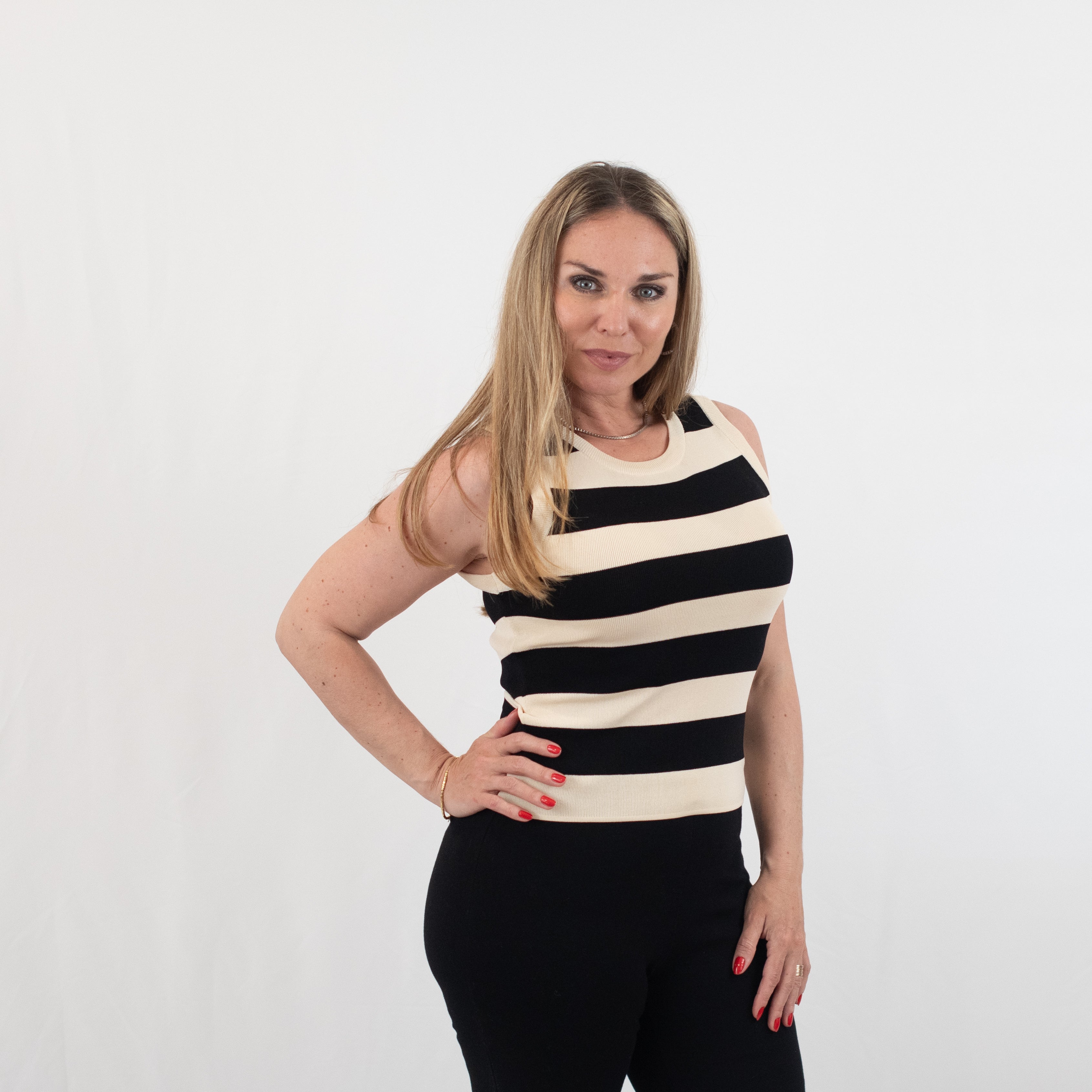 Side view of a woman wearing a sleeveless black and white striped knit top with black pants, showcasing a sleek and stylish outfit.