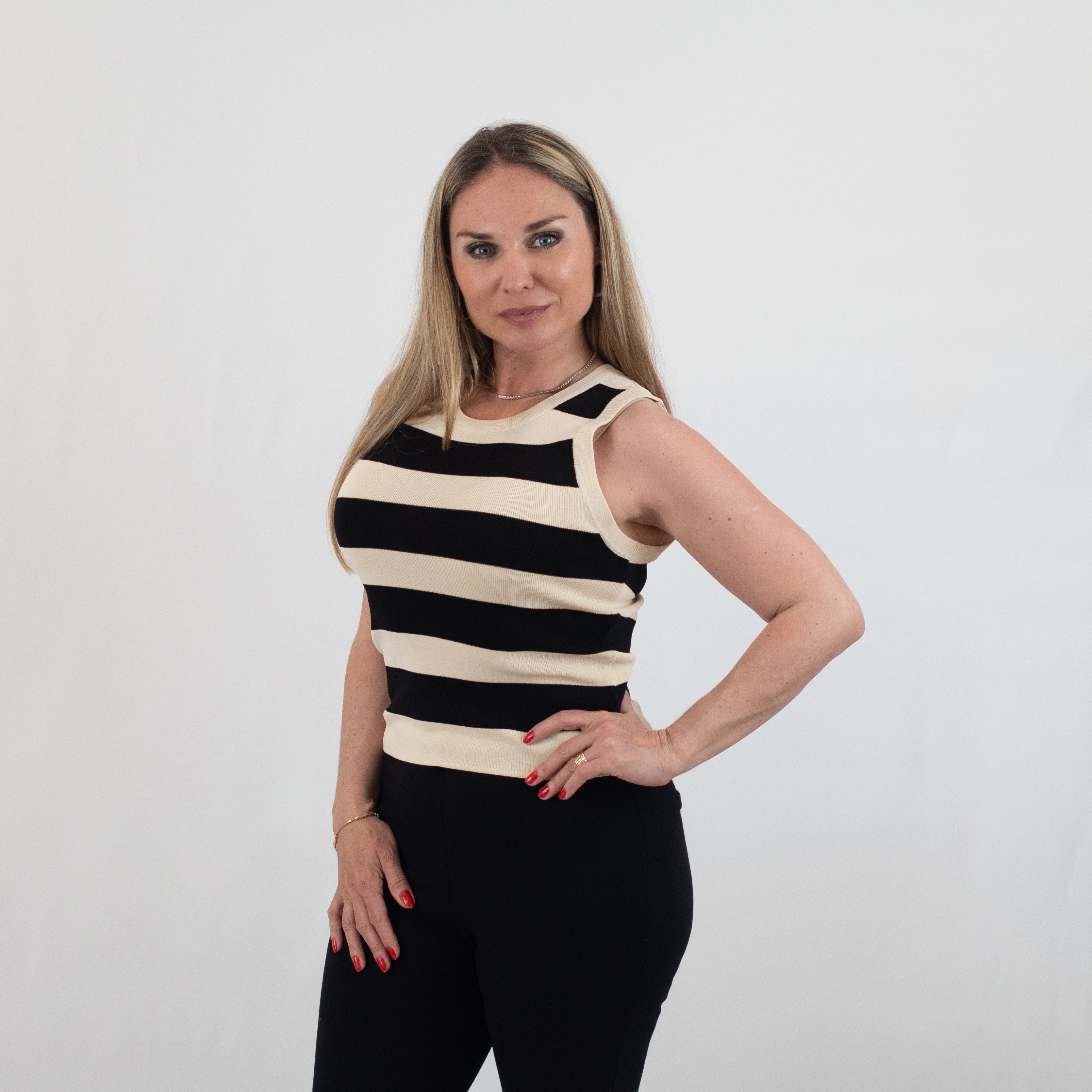 Woman wearing a black and white striped sleeveless knit top styled with black trousers for a modern casual look.