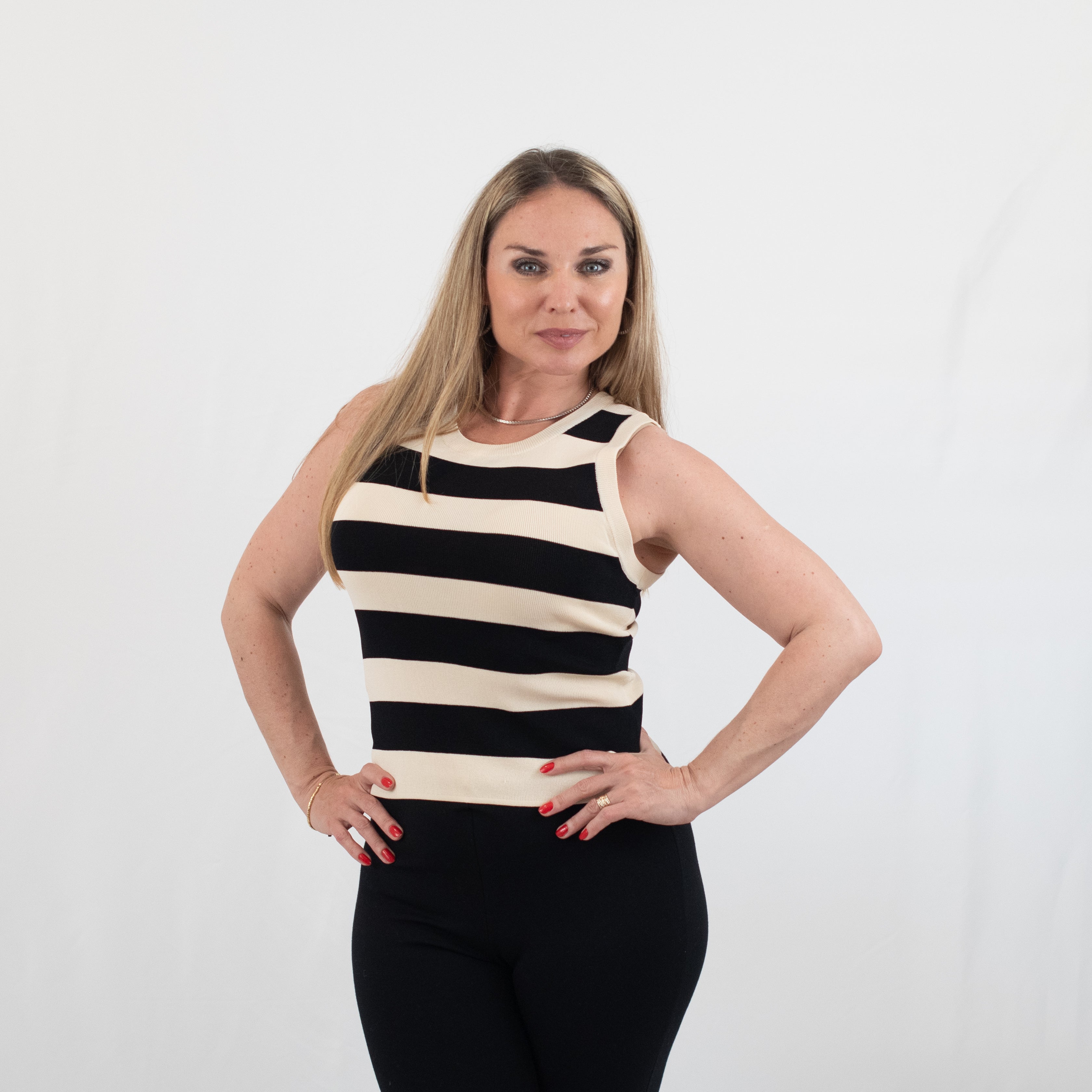 Woman modeling a sleeveless black and white striped knit top paired with fitted black pants, styled for a chic casual look.