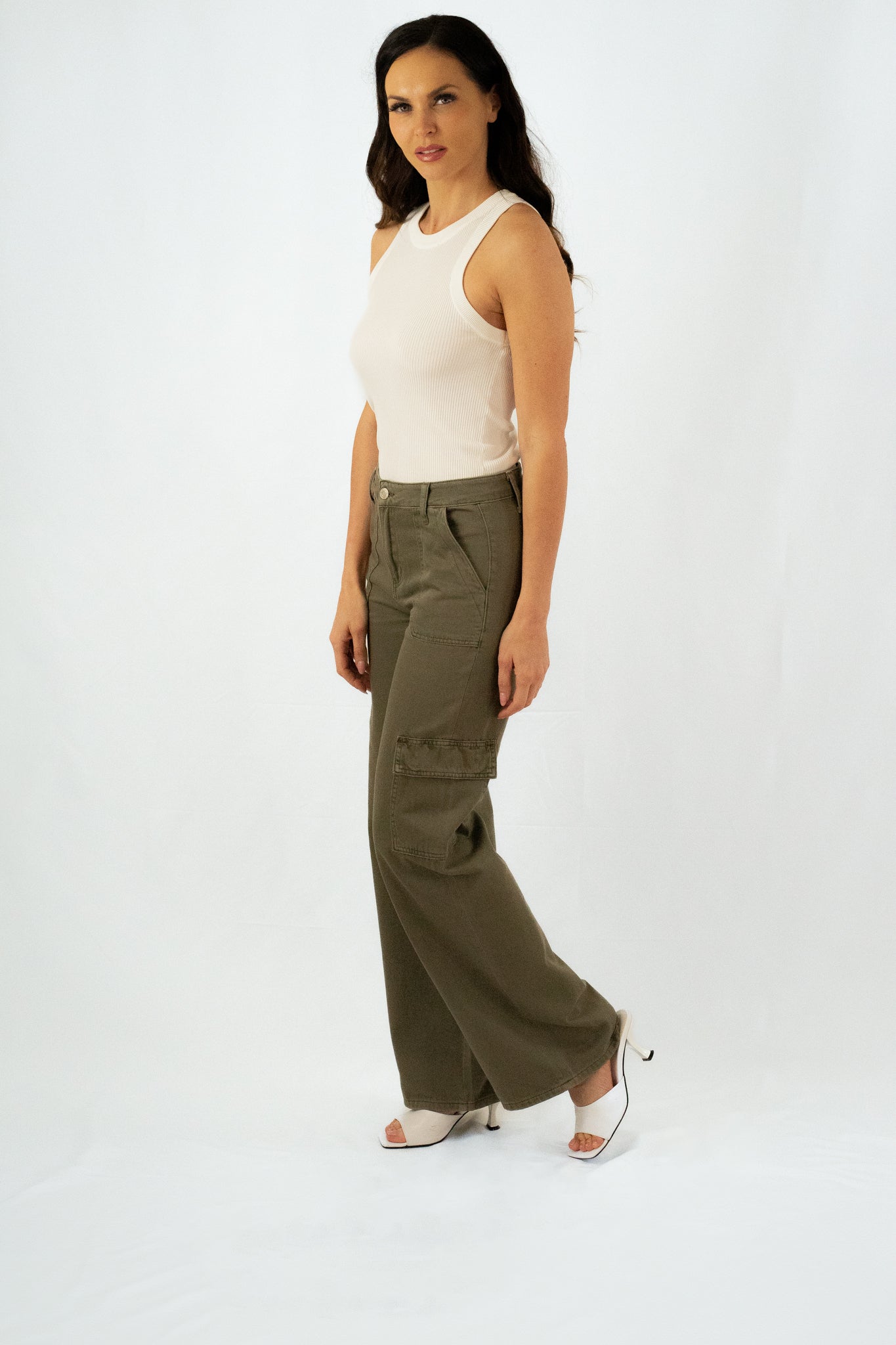 Woman wearing olive green wide-leg cargo pants with multiple pockets, paired with a white ribbed tank top and white open-toe heels.