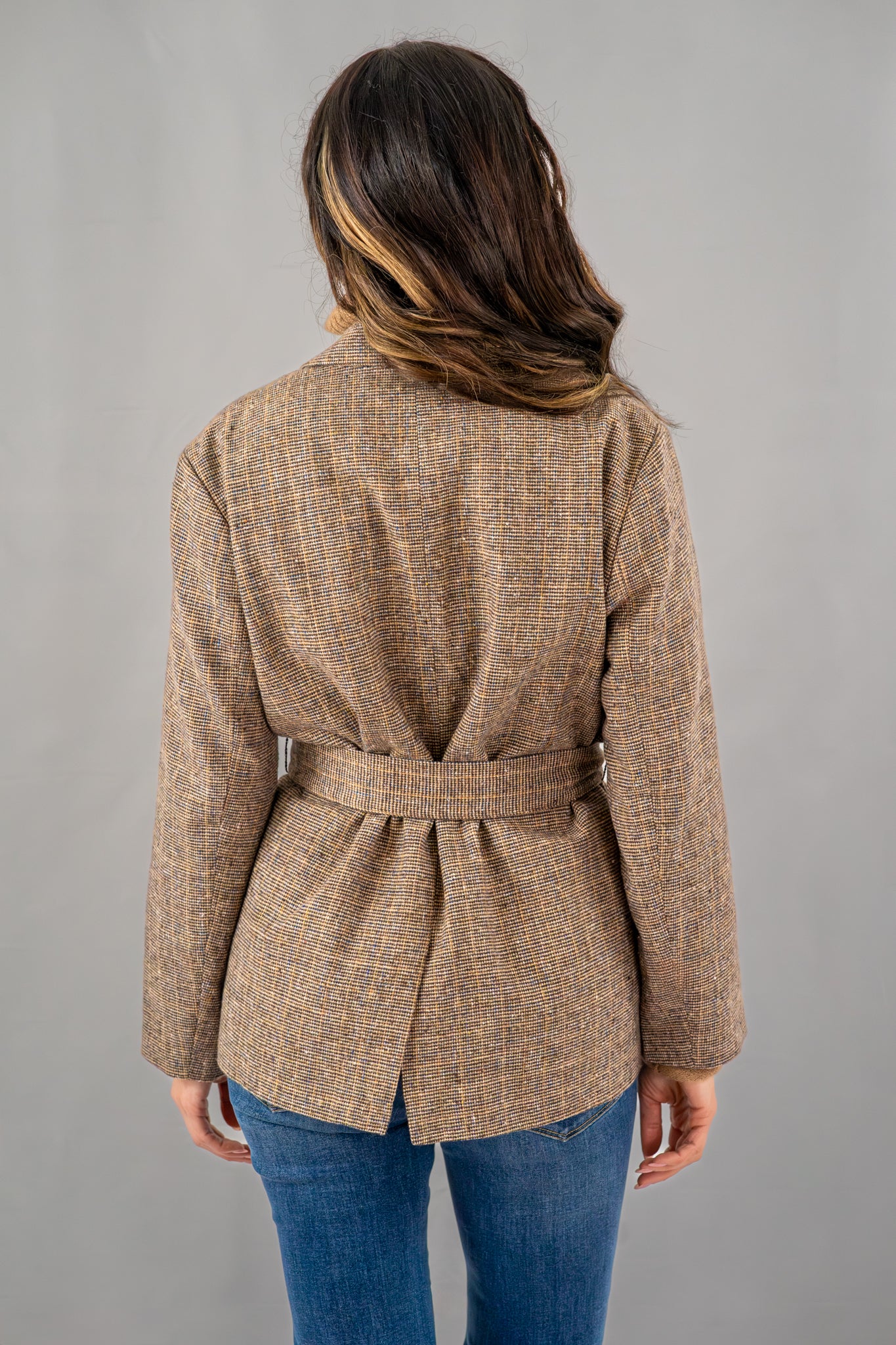  Back view of a brown belted blazer with tailored detailing, paired with blue flared jeans for a versatile outfit.

