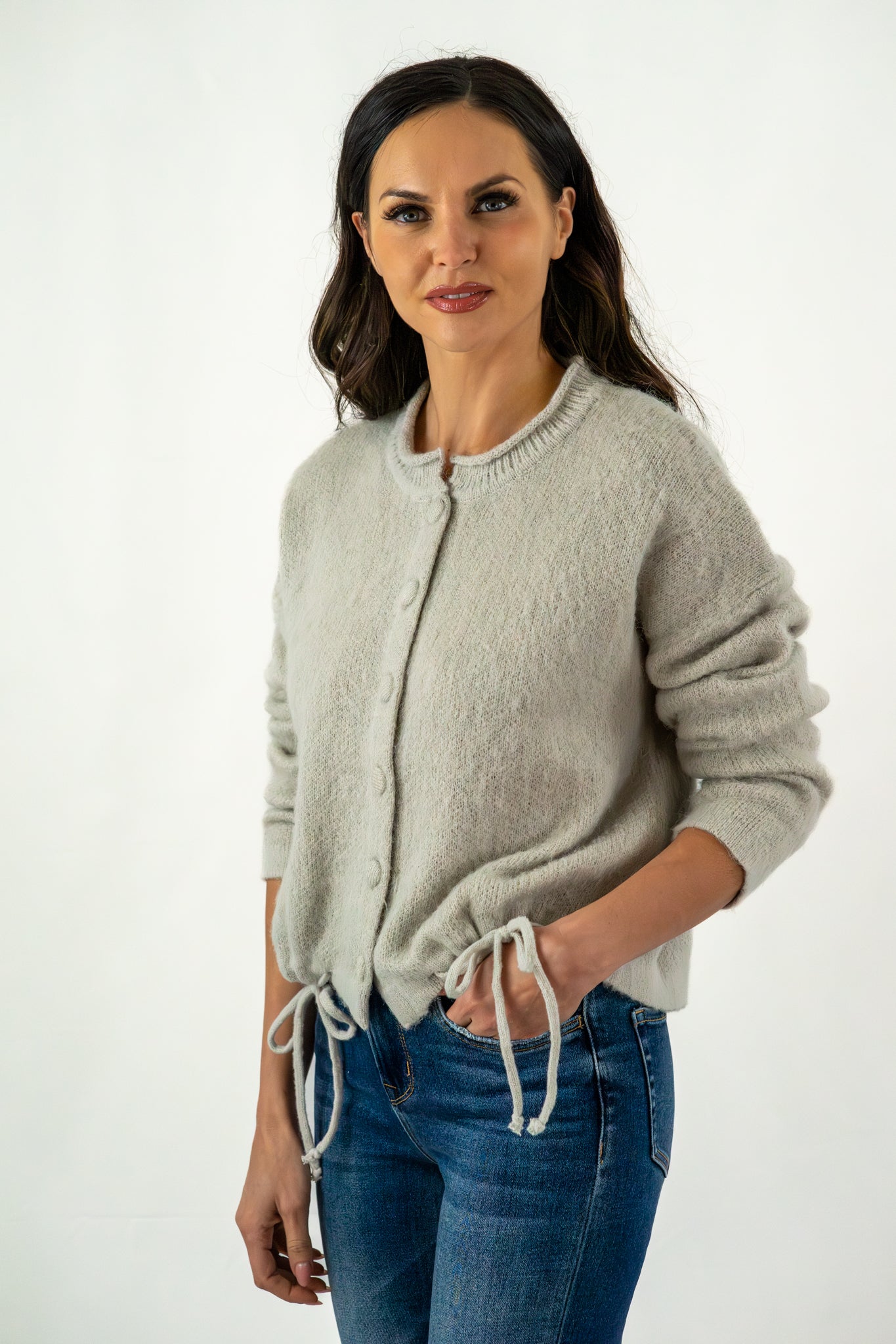 Woman wearing a soft grey button-up cardigan with drawstring details, styled with blue denim jeans for a cozy and casual look.