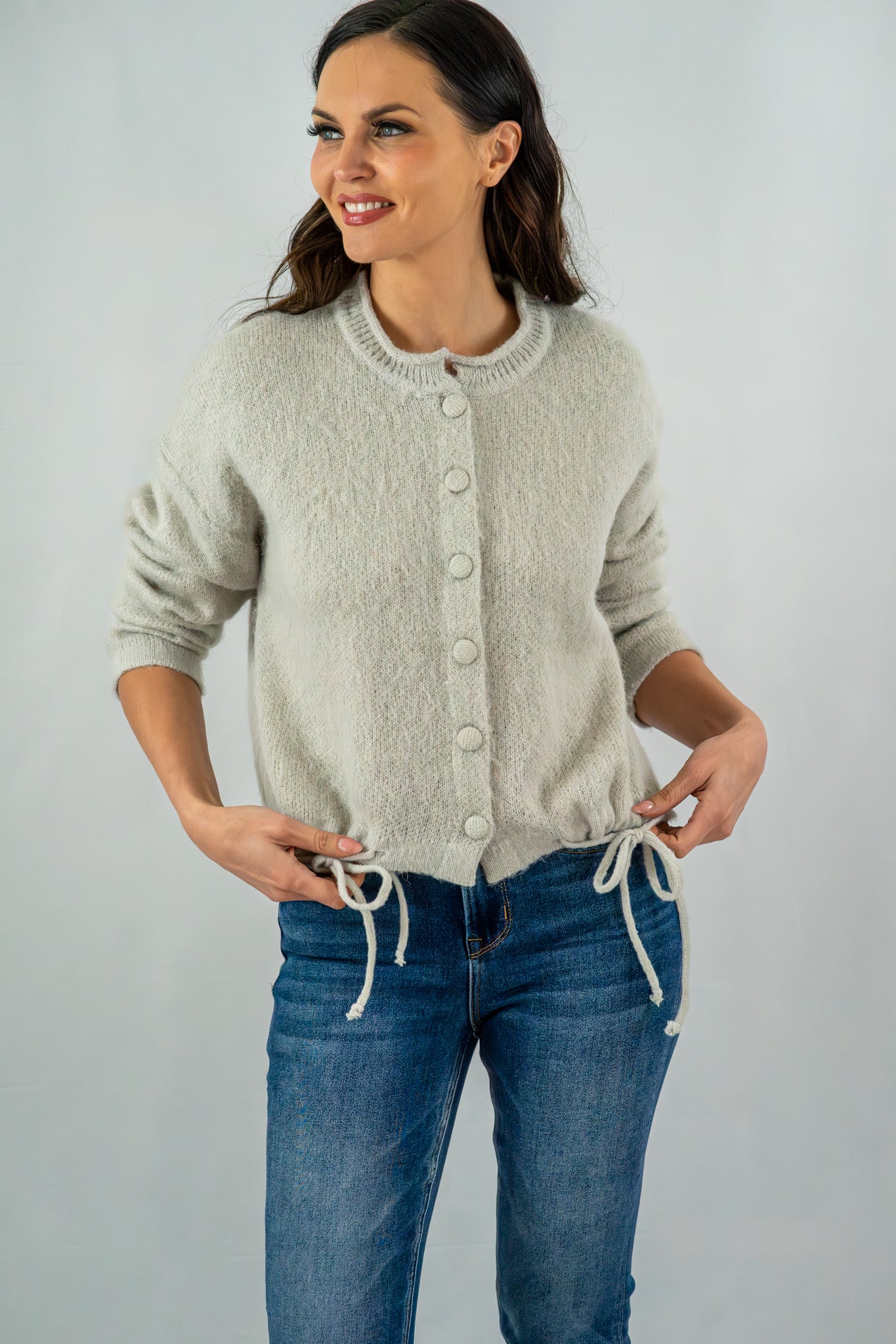 Close-up of a grey button-front cardigan featuring drawstring accents at the hem, paired with blue jeans for a relaxed outfit.