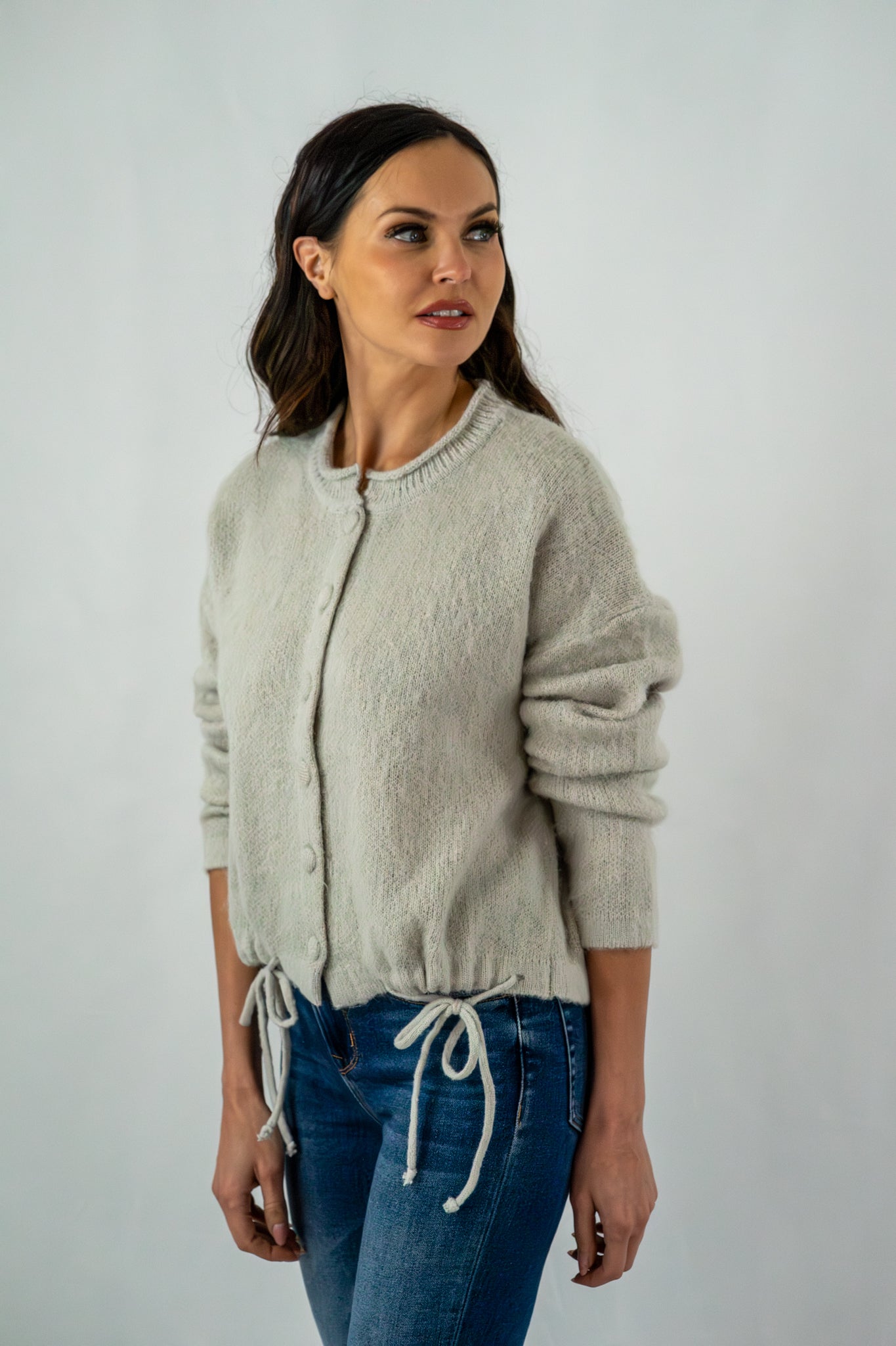 Side view of a woman in a grey button-up cardigan with adjustable drawstring details, styled casually with jeans.