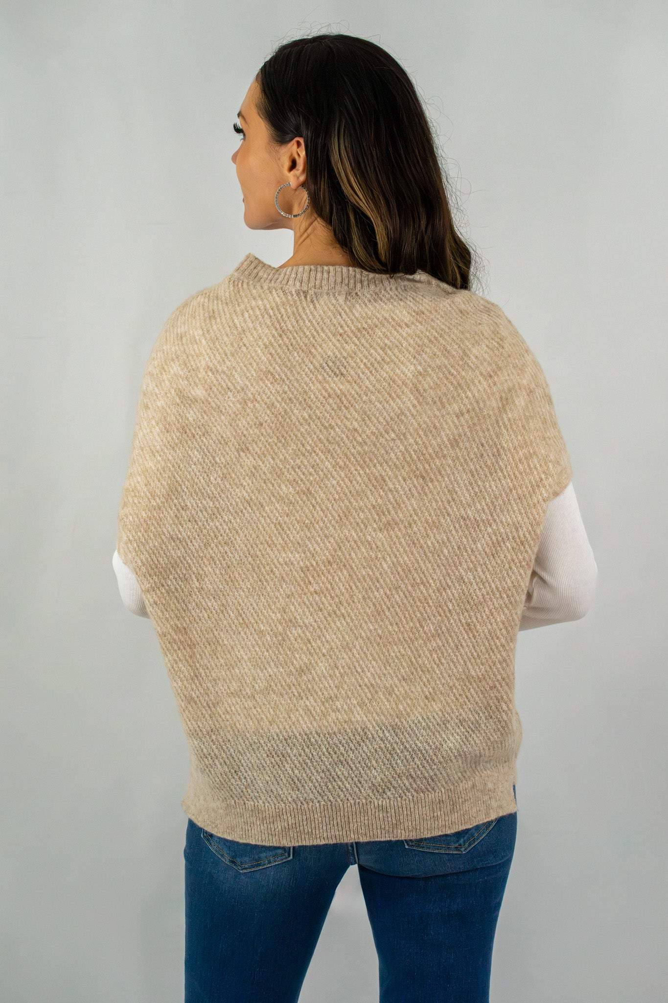 Back view of a beige short-sleeve knit sweater layered over a white long-sleeve top, styled with blue jeans for a cozy outfit.