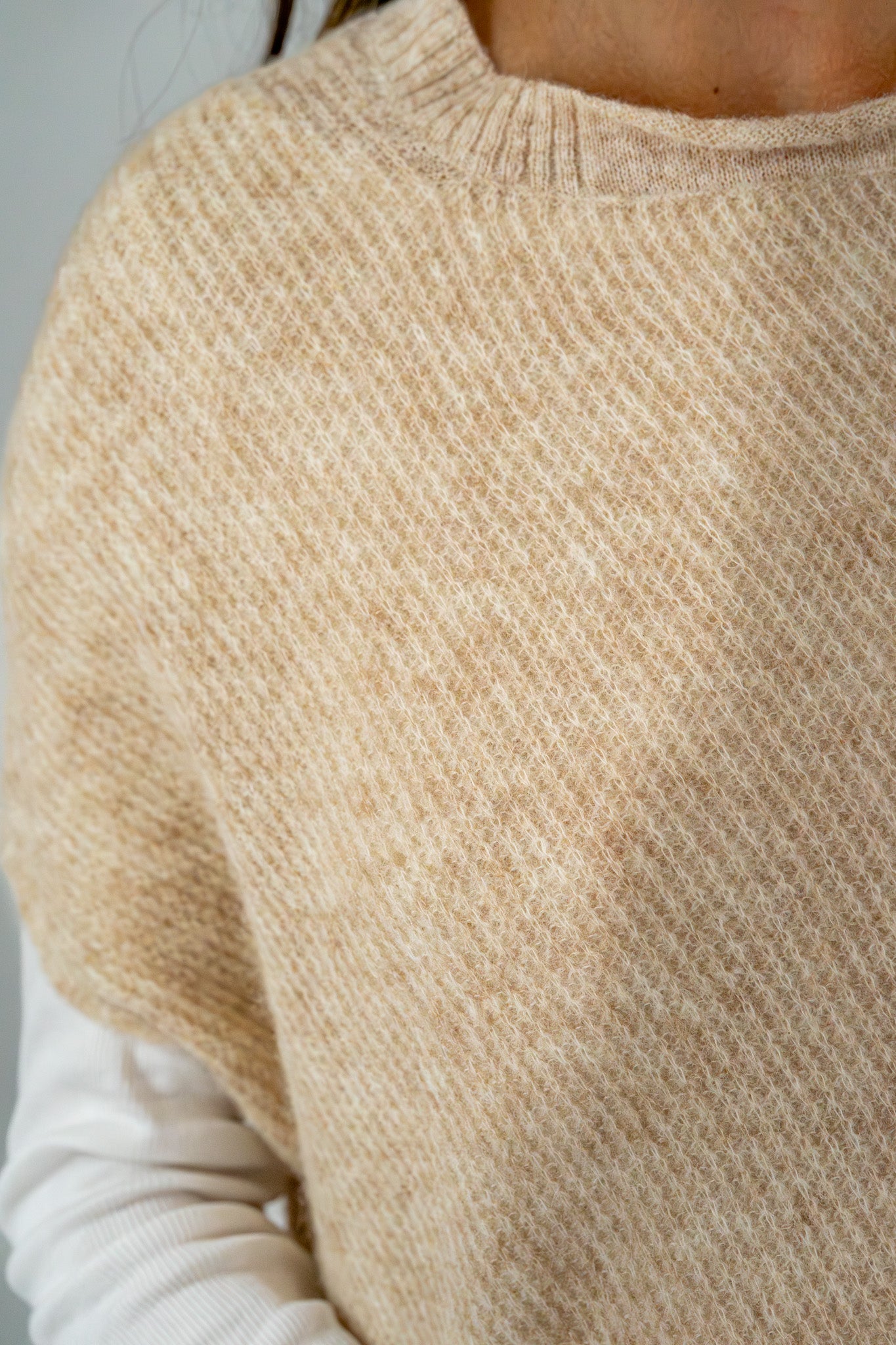  Close-up of the textured knit fabric of a beige sweater, highlighting its soft material and subtle pattern.