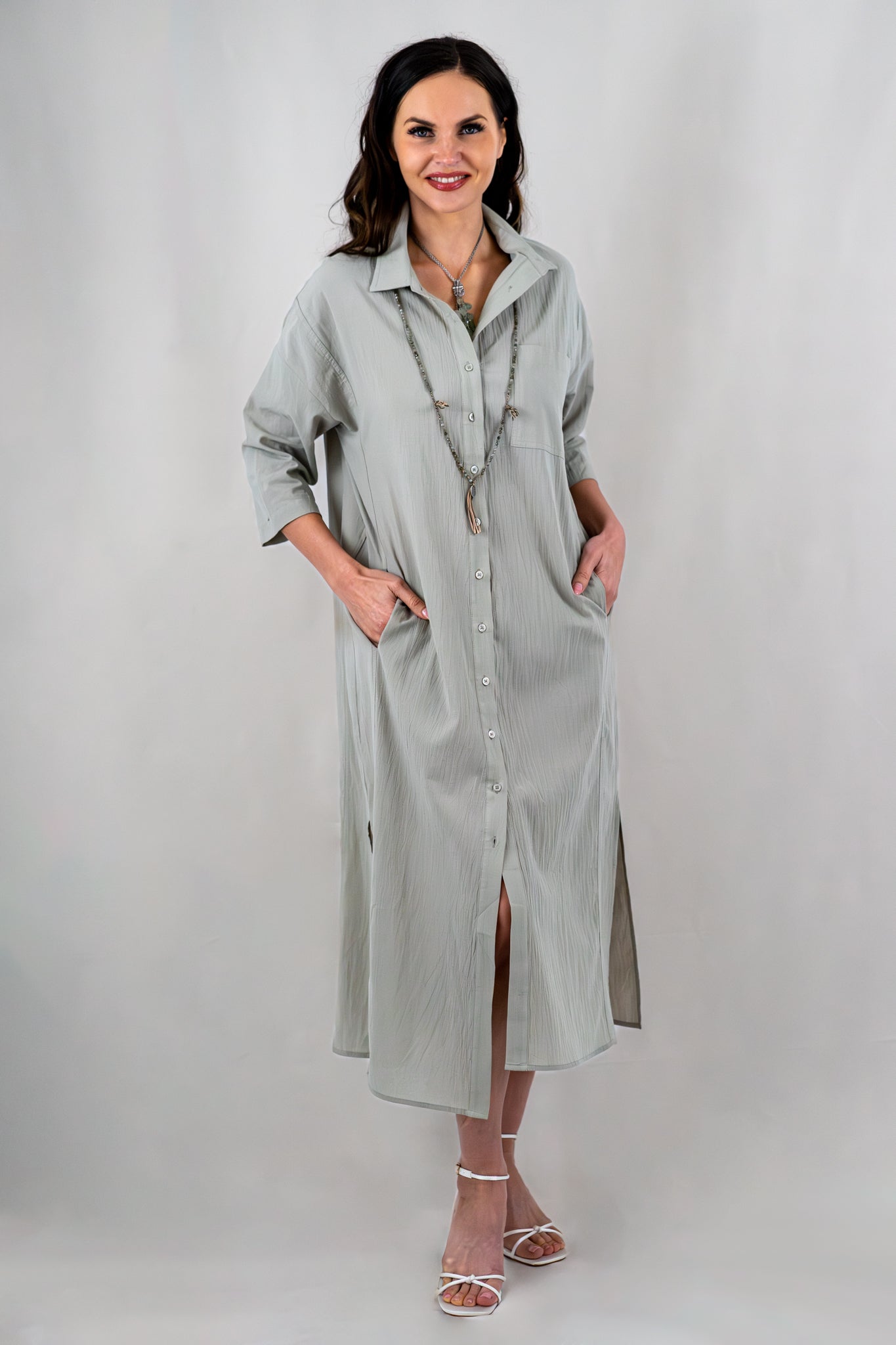 Sage green collared midi dress styled with side slits and buttons down the front, featuring relaxed 3/4 sleeves and accessorized with necklaces and heels.