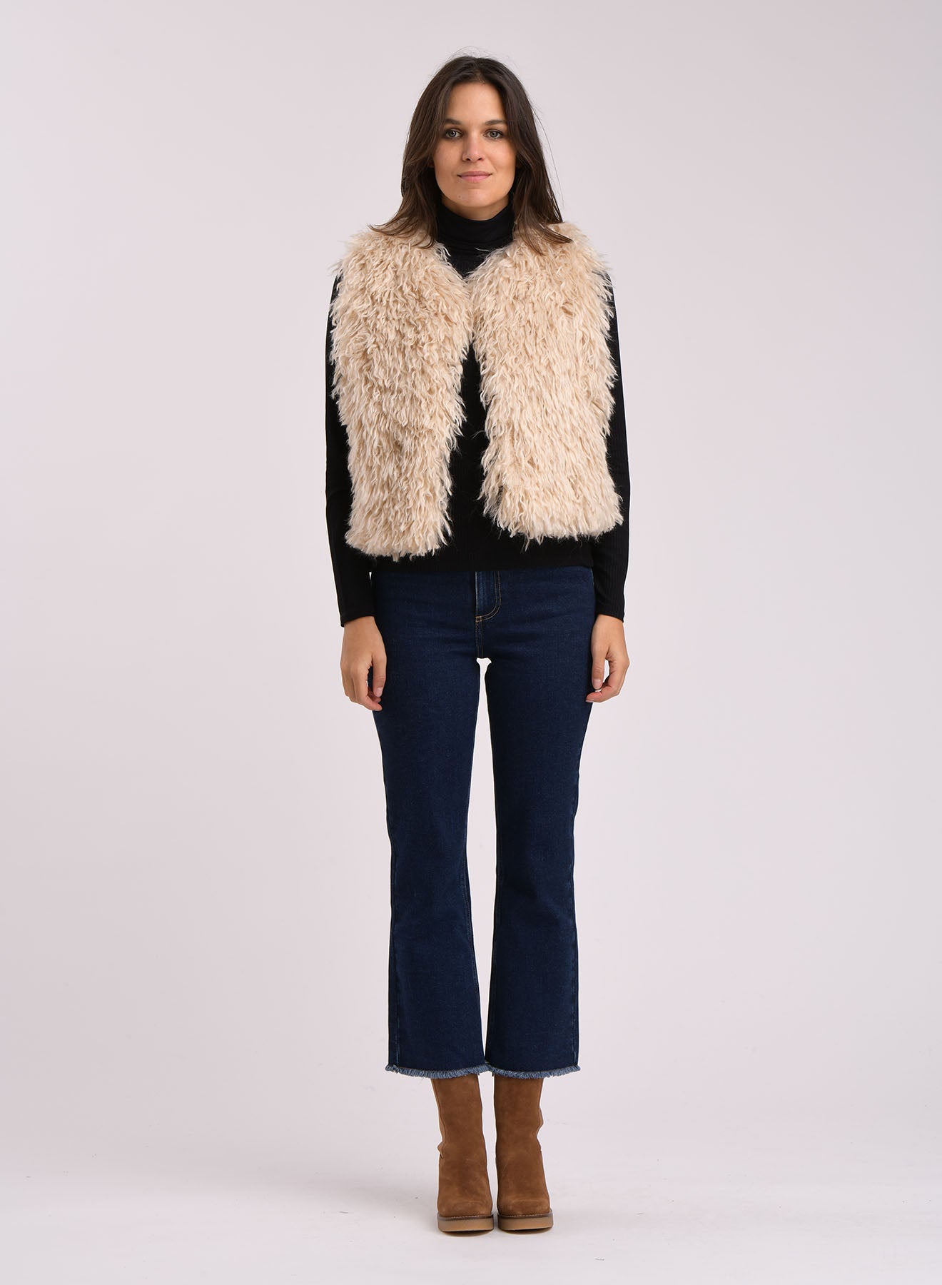 Zoani Sleeveless Jacket in beige faux shearling, paired with a black turtleneck and flared jeans.