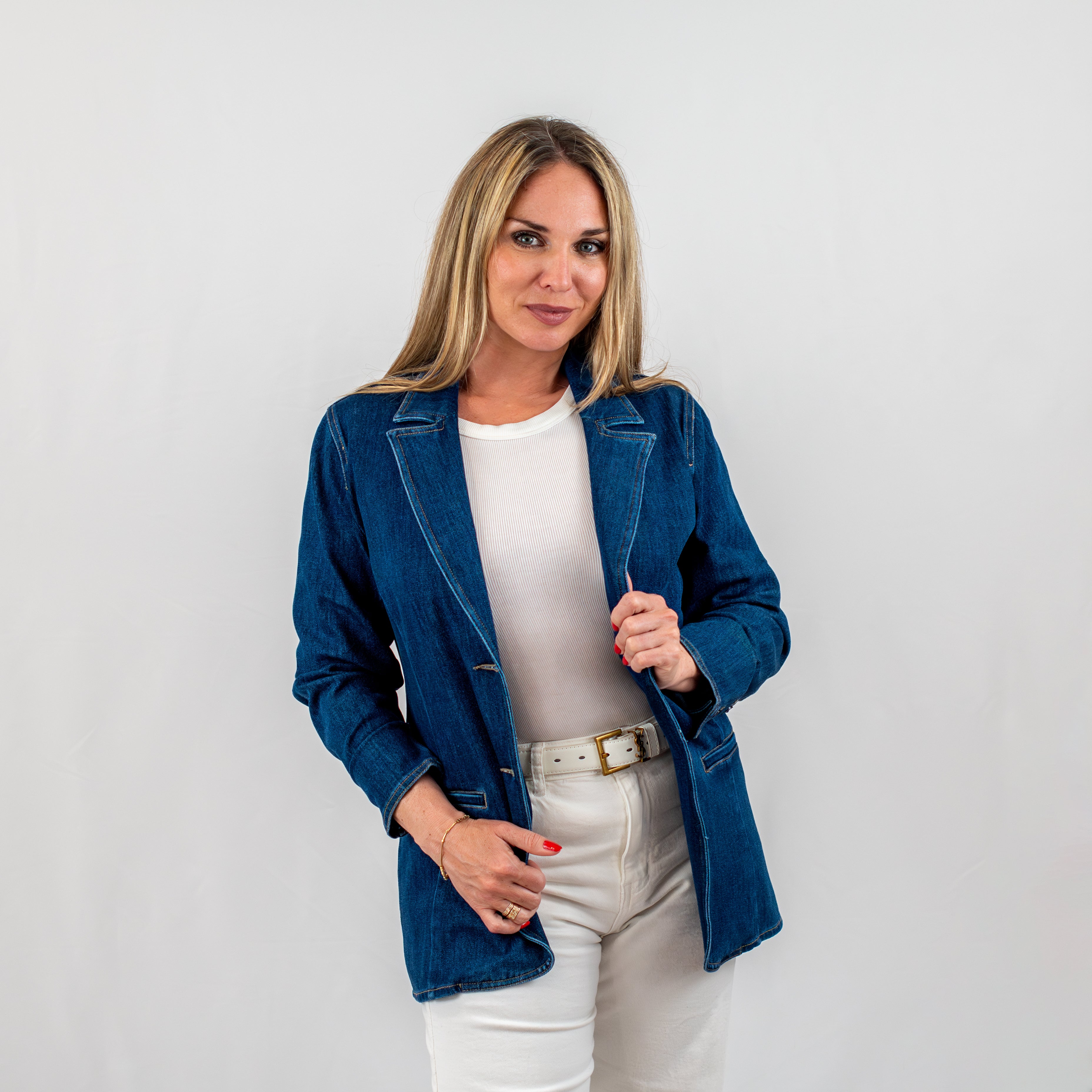 Woman wearing a tailored denim blazer over a white top, styled with white jeans and a belt, perfect for a chic casual look.