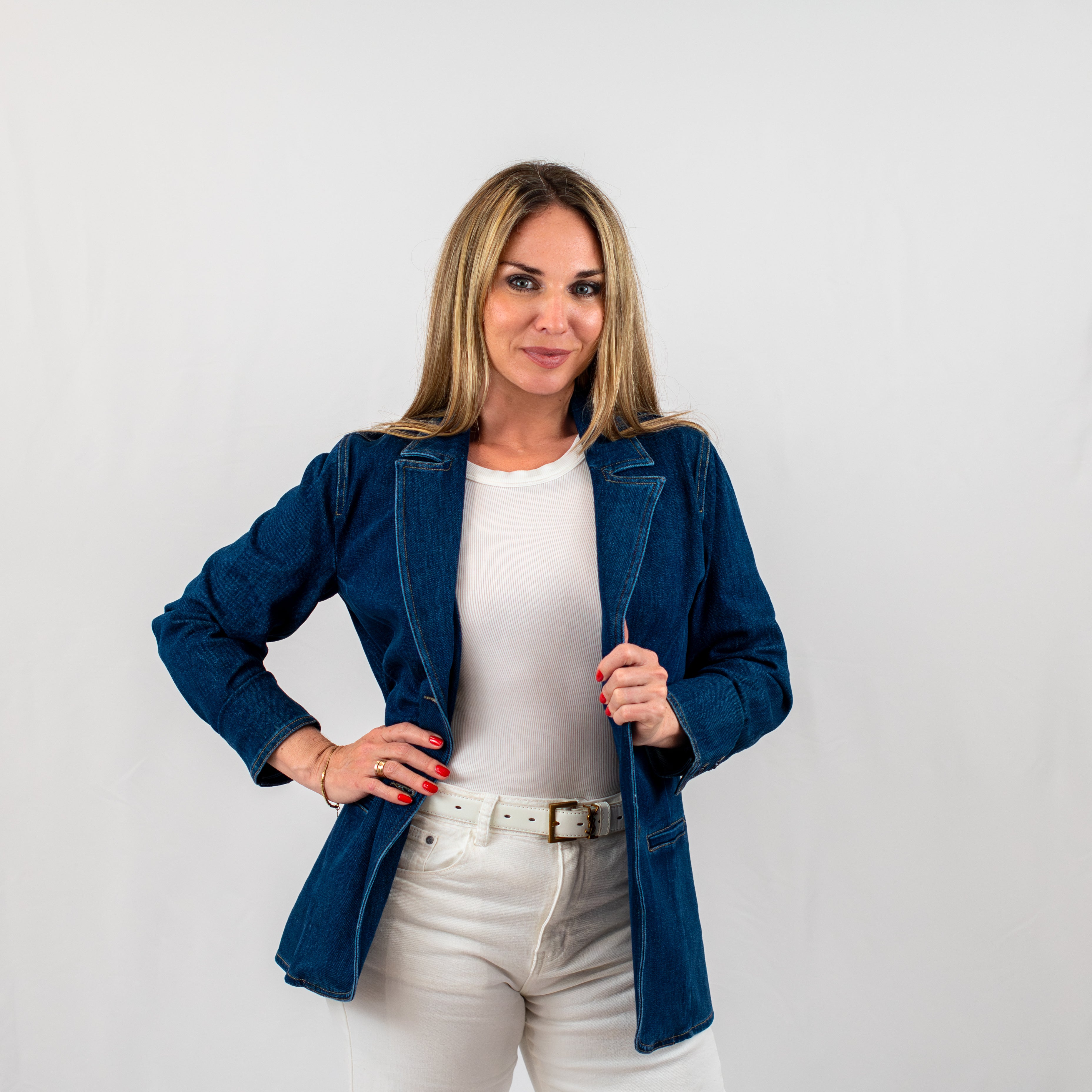 Front view of a woman modeling a fitted denim blazer paired with a white shirt and white jeans, showcasing a polished yet relaxed outfit.