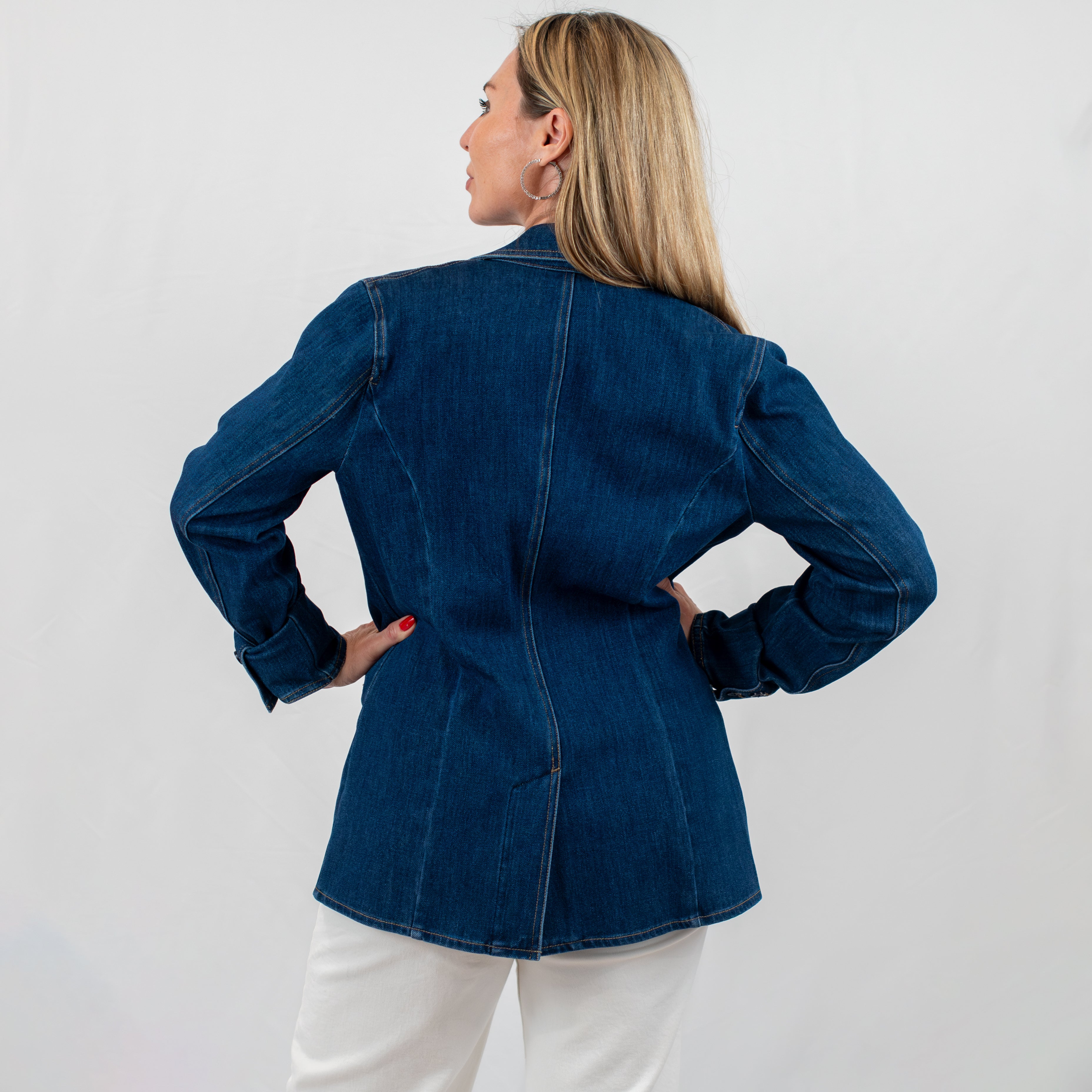 Back view of a tailored denim blazer, highlighting the detailed stitching and flattering fit, paired with white trousers.