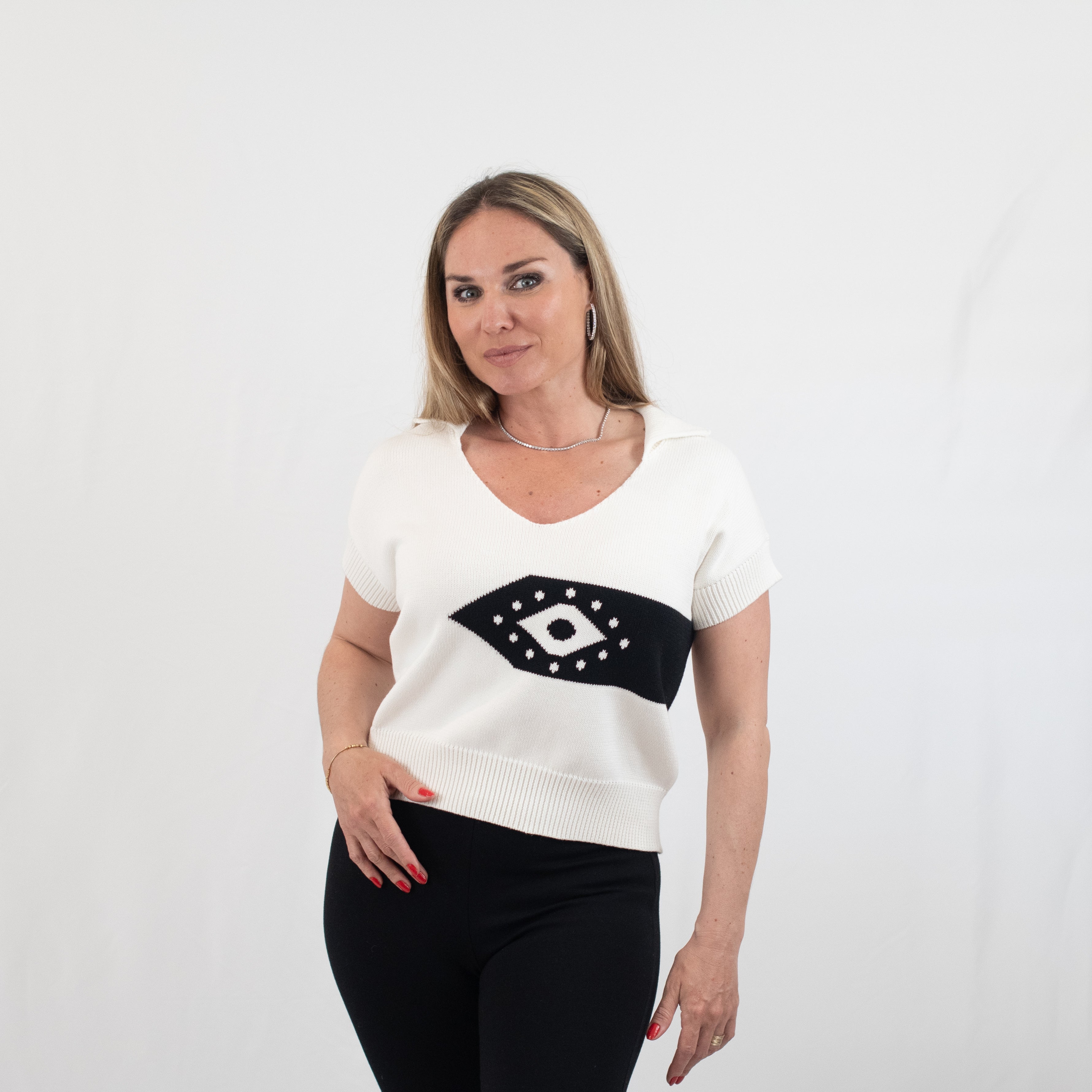 Woman wearing the Ada short sleeve V-neck jumper in white with black eye motif, made of 100% organic cotton, showcasing the front view with a relaxed fit and ribbed hem.