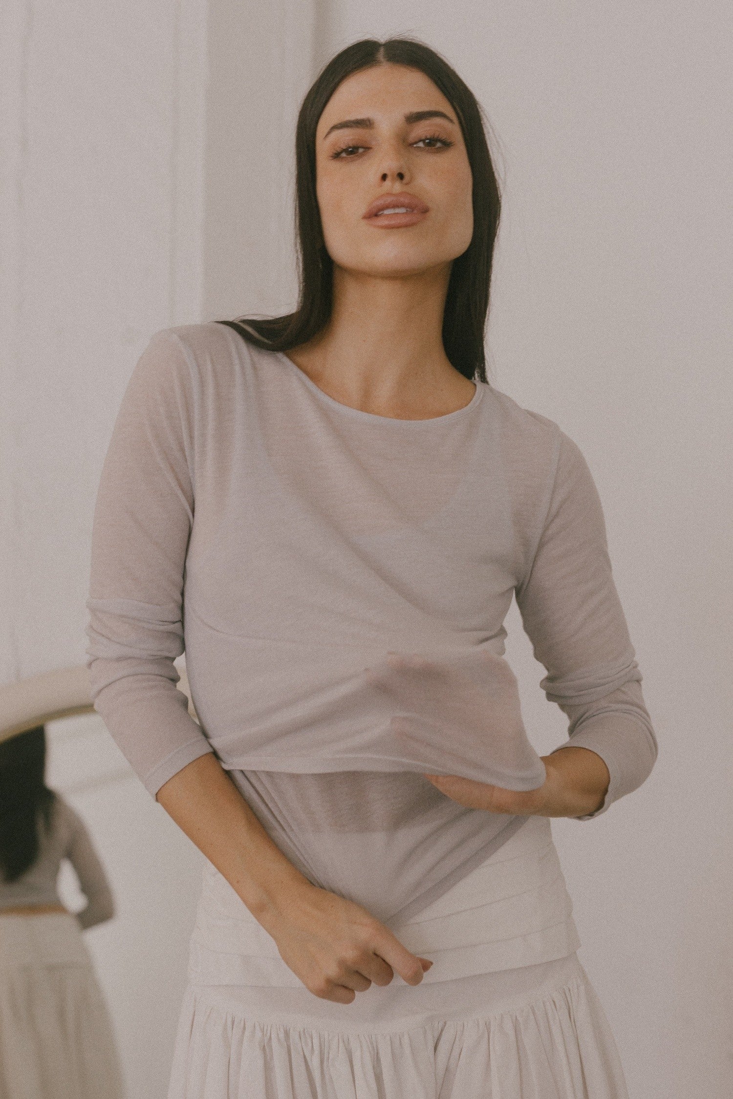 Woman wearing a sheer grey long-sleeve top and tiered white skirt, highlighting the lightweight and translucent fabric.