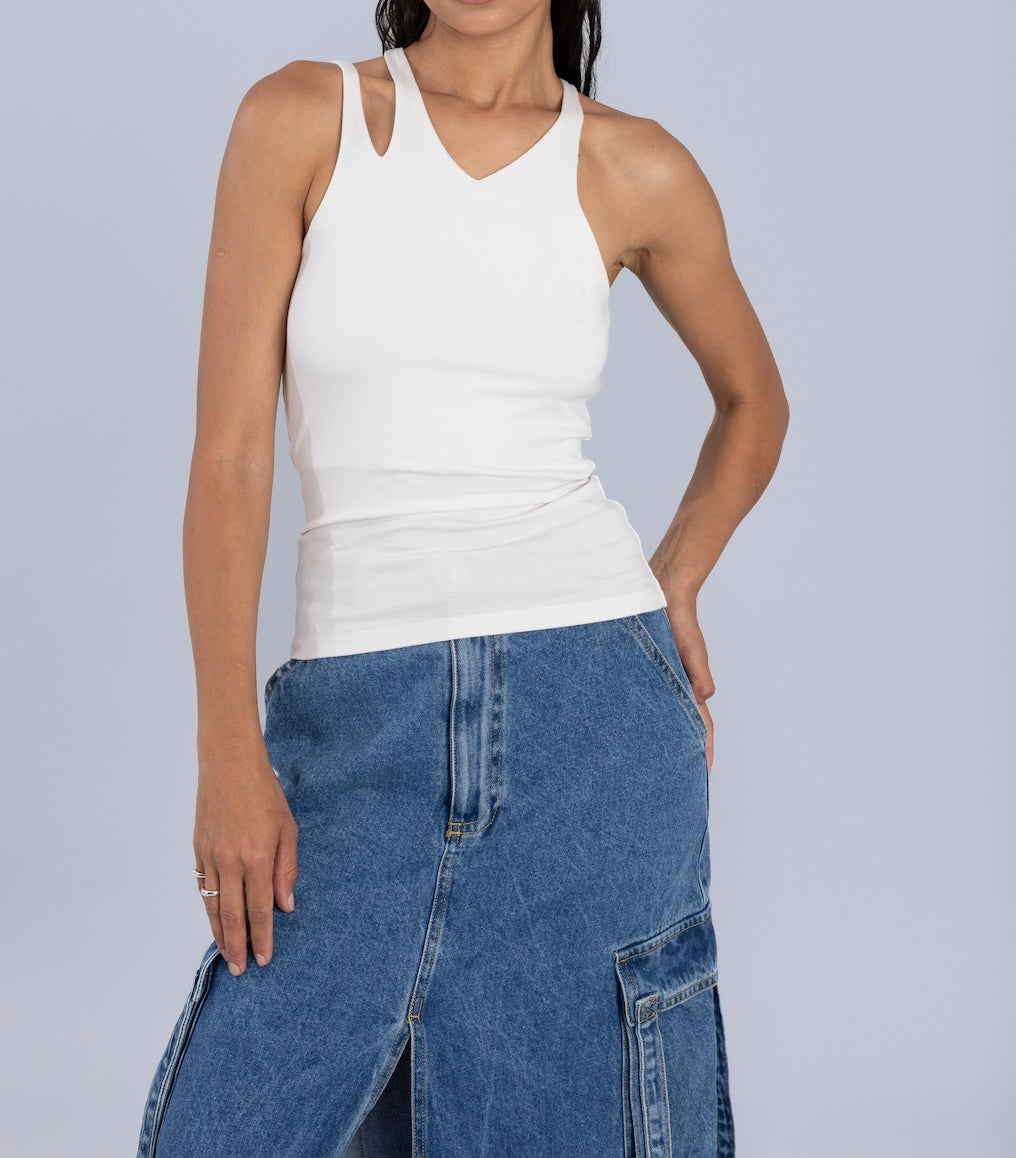 Woman wearing a white racerback tank top paired with a blue denim midi skirt featuring front cargo-style pockets and a slit, standing against a light gray background.