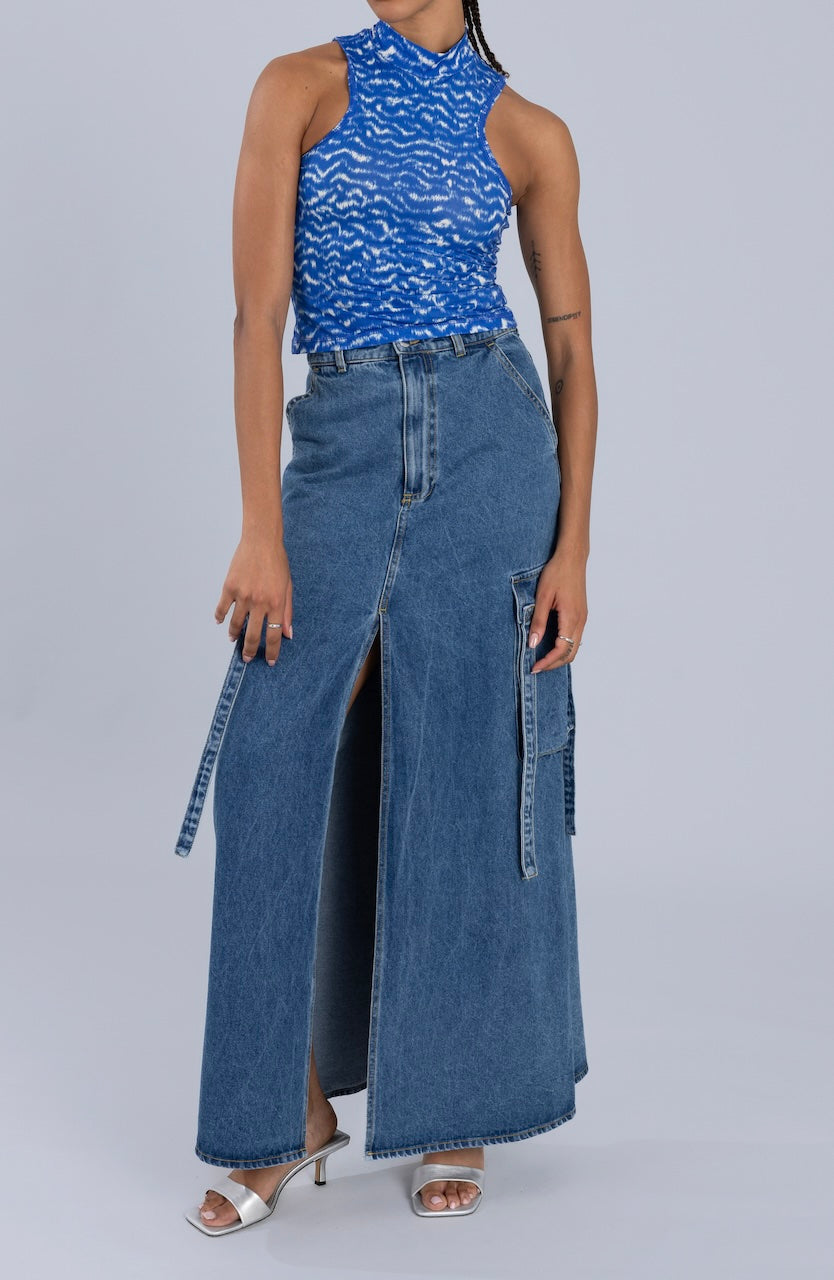 Woman wearing a high-waisted blue maxi denim skirt with cargo pockets and front slit, paired with a sleeveless blue patterned top and silver heels.