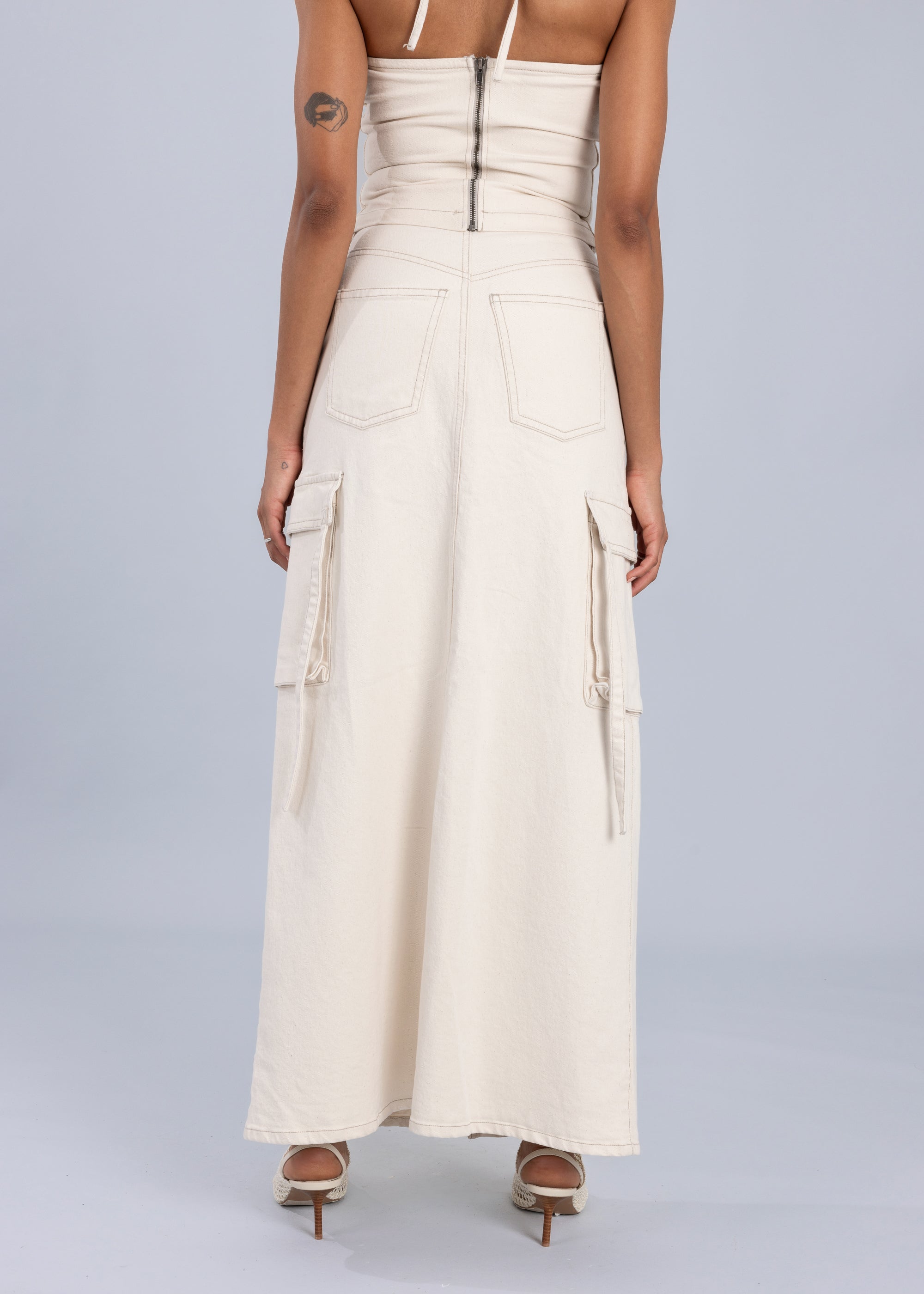 Back view of a white maxi denim skirt with utility-inspired details and back pockets, paired with a cream sleeveless top.