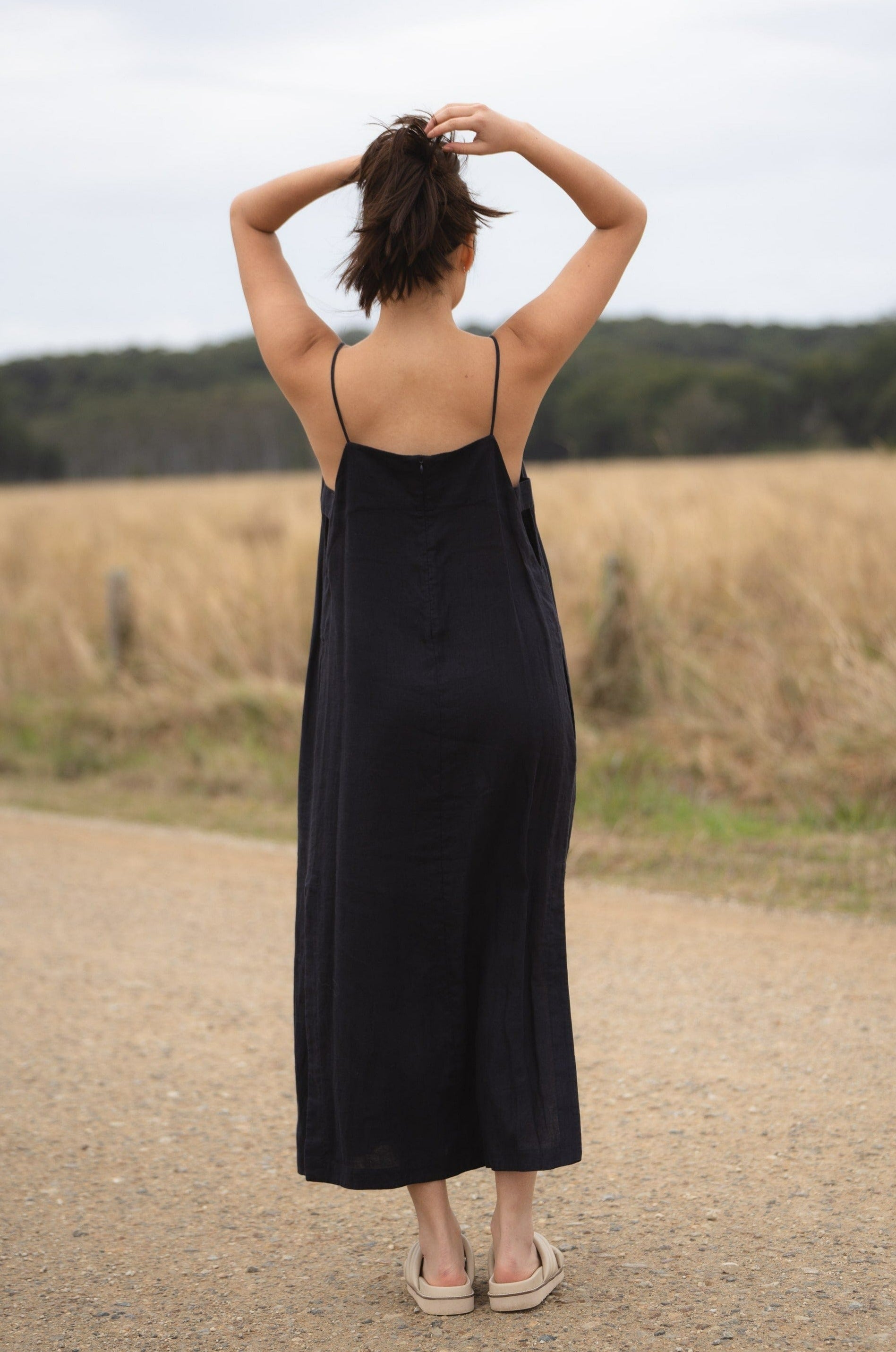 Back view of the Kai linen navy dress featuring slender straps converging at the center, with a flowing silhouette down to a mid-calf hem.